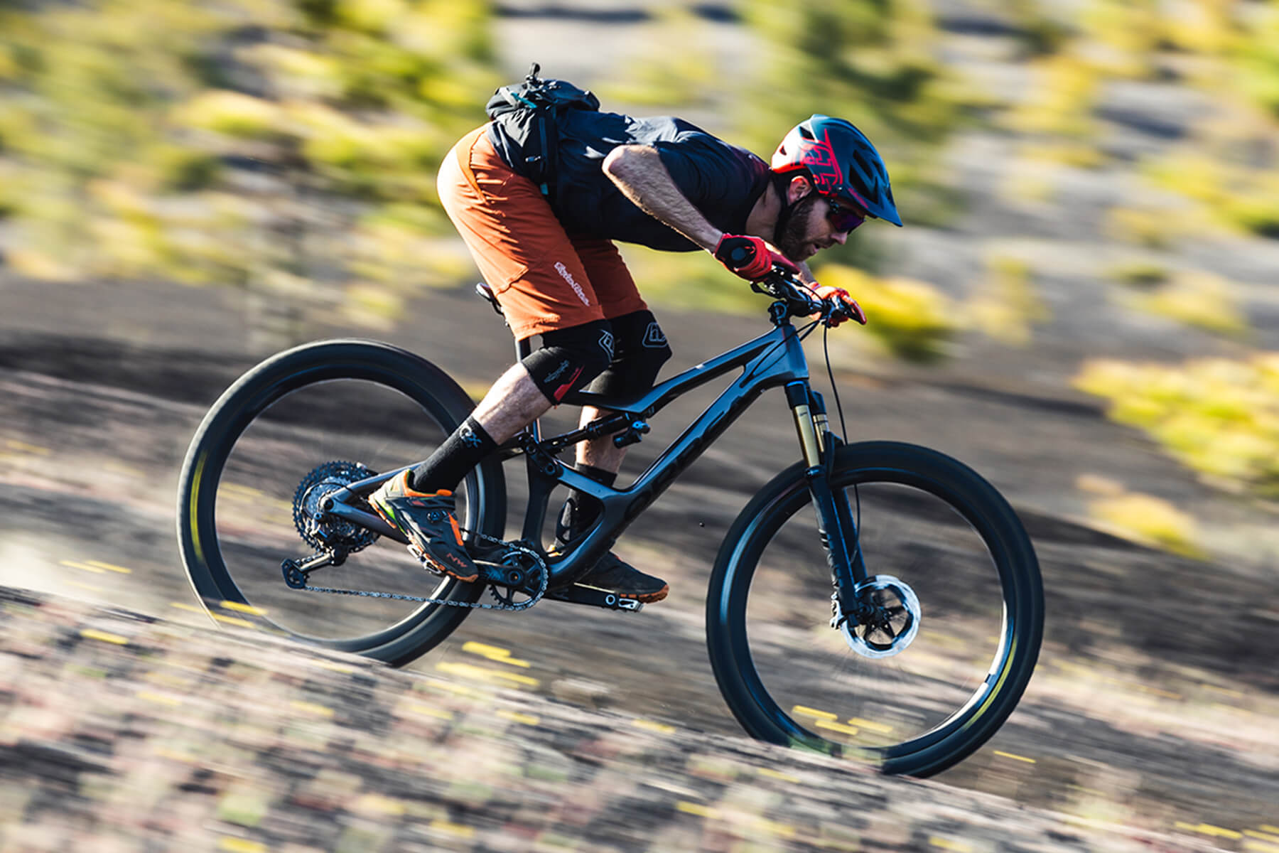 A Man on a black Orbea Occam descending a mountain bike trail very fast. 