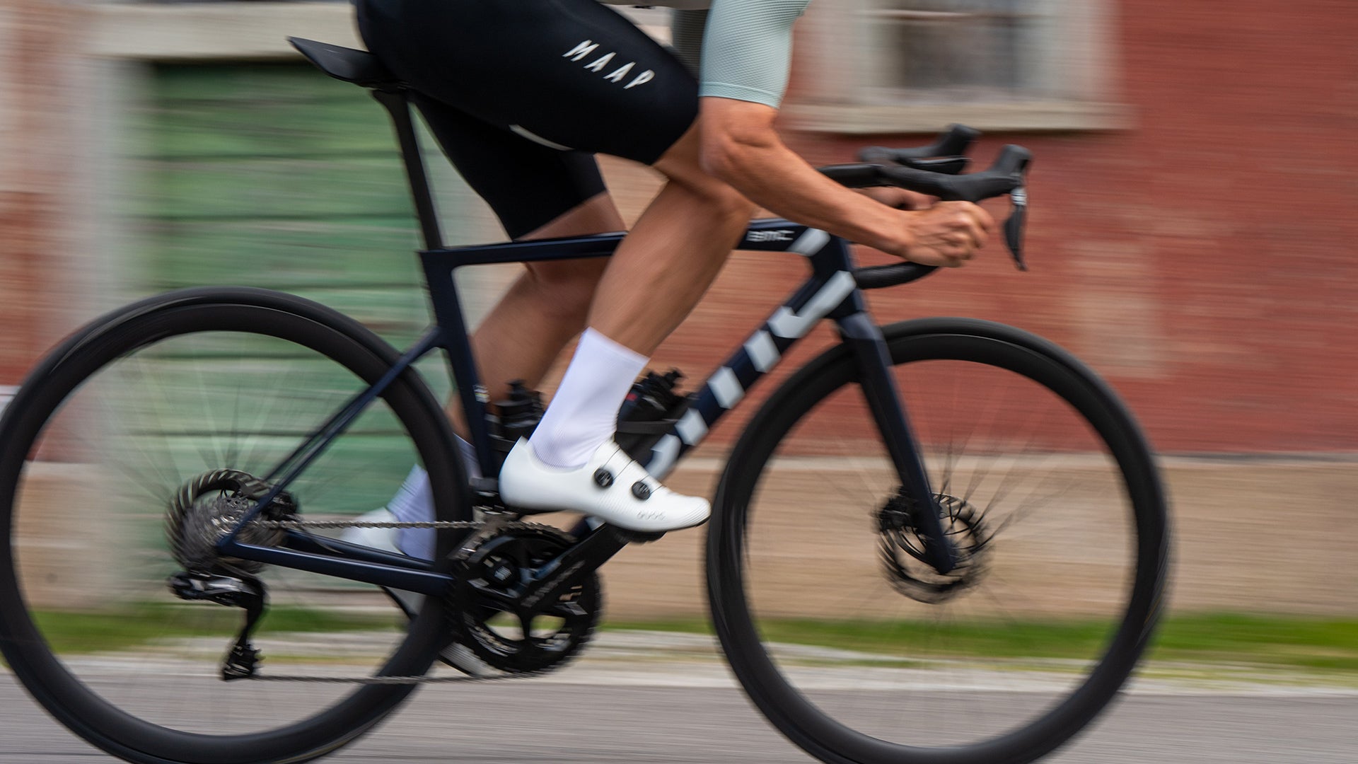 A Man riding a BMC road bike against a brick wall.