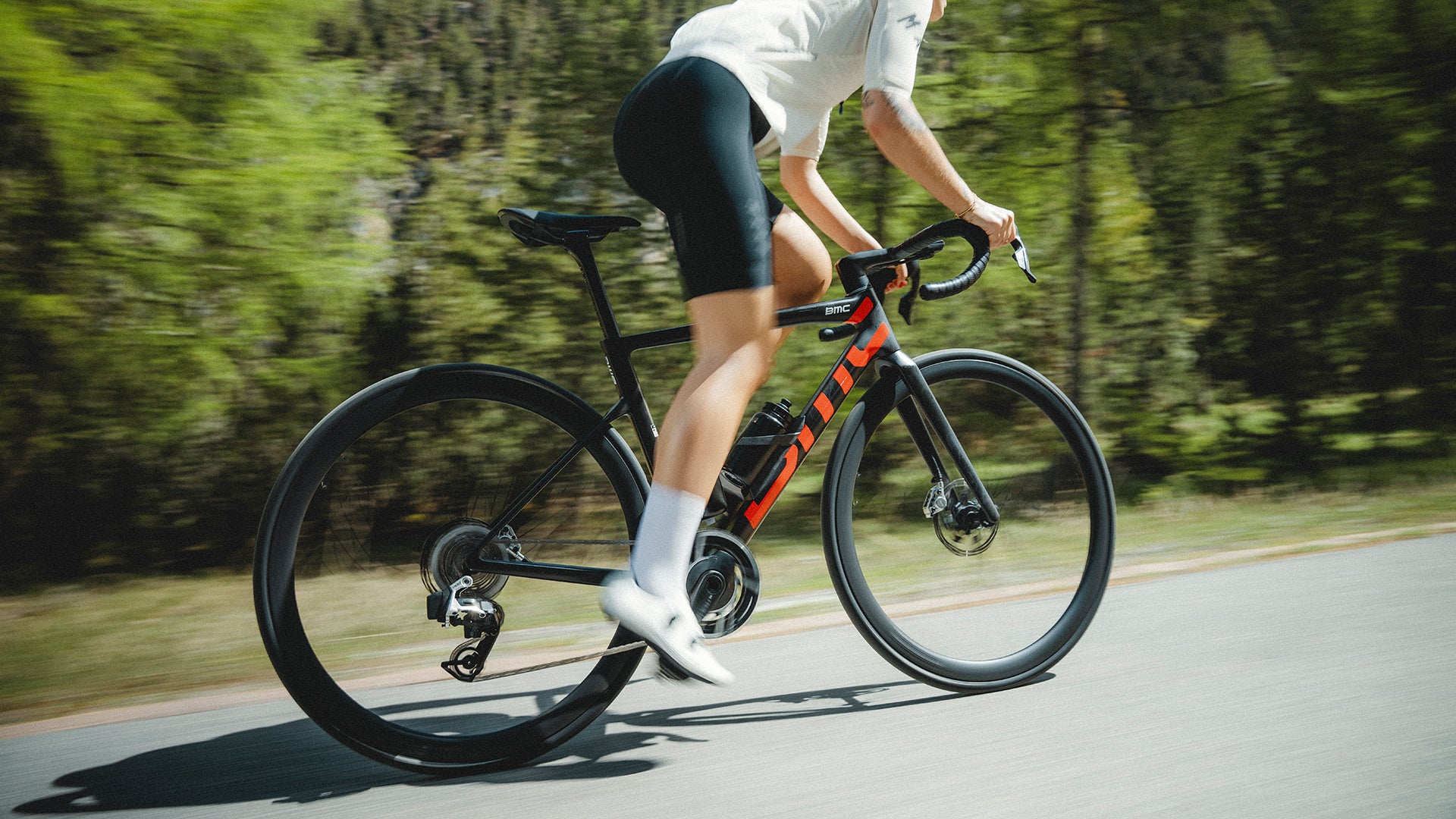 A man riding a BMC teammachine road bike up a hill in a forest. 