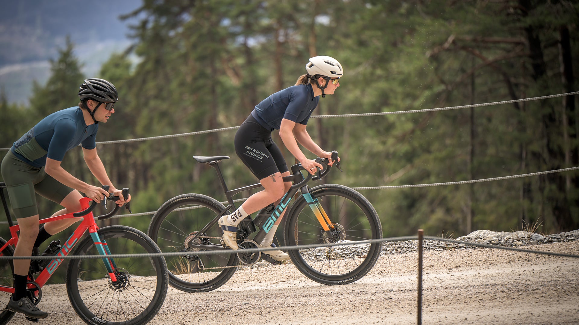 A man and a woman riding the BMC kaius gravel race bike up a dirt hill. 