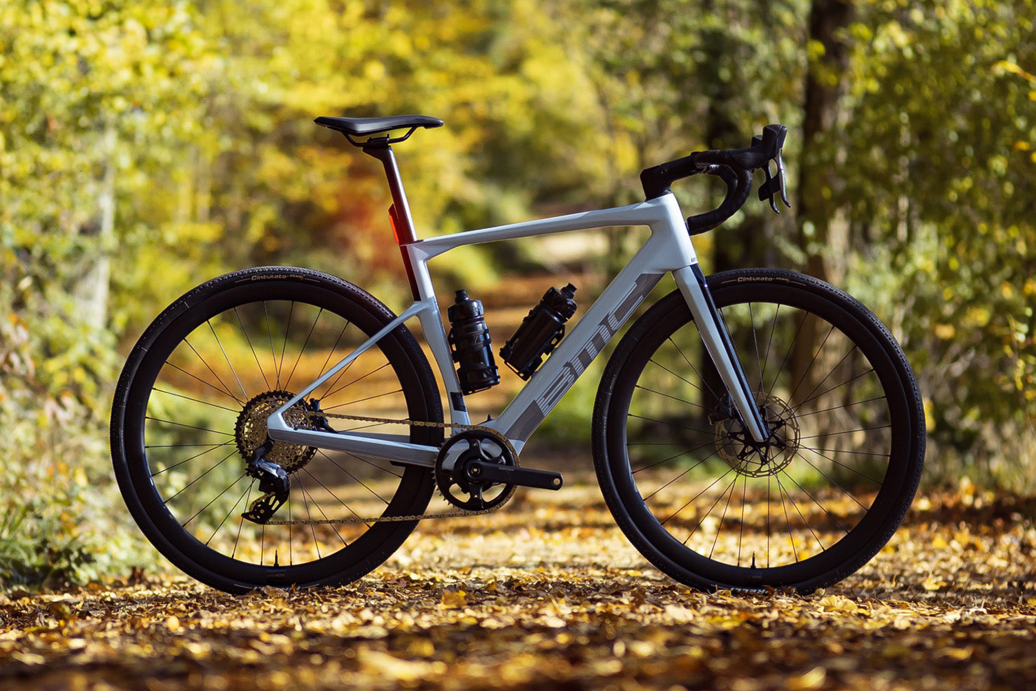A Silver BMC Roadmachine AMP  electric Road Bike photographed against a forest. 