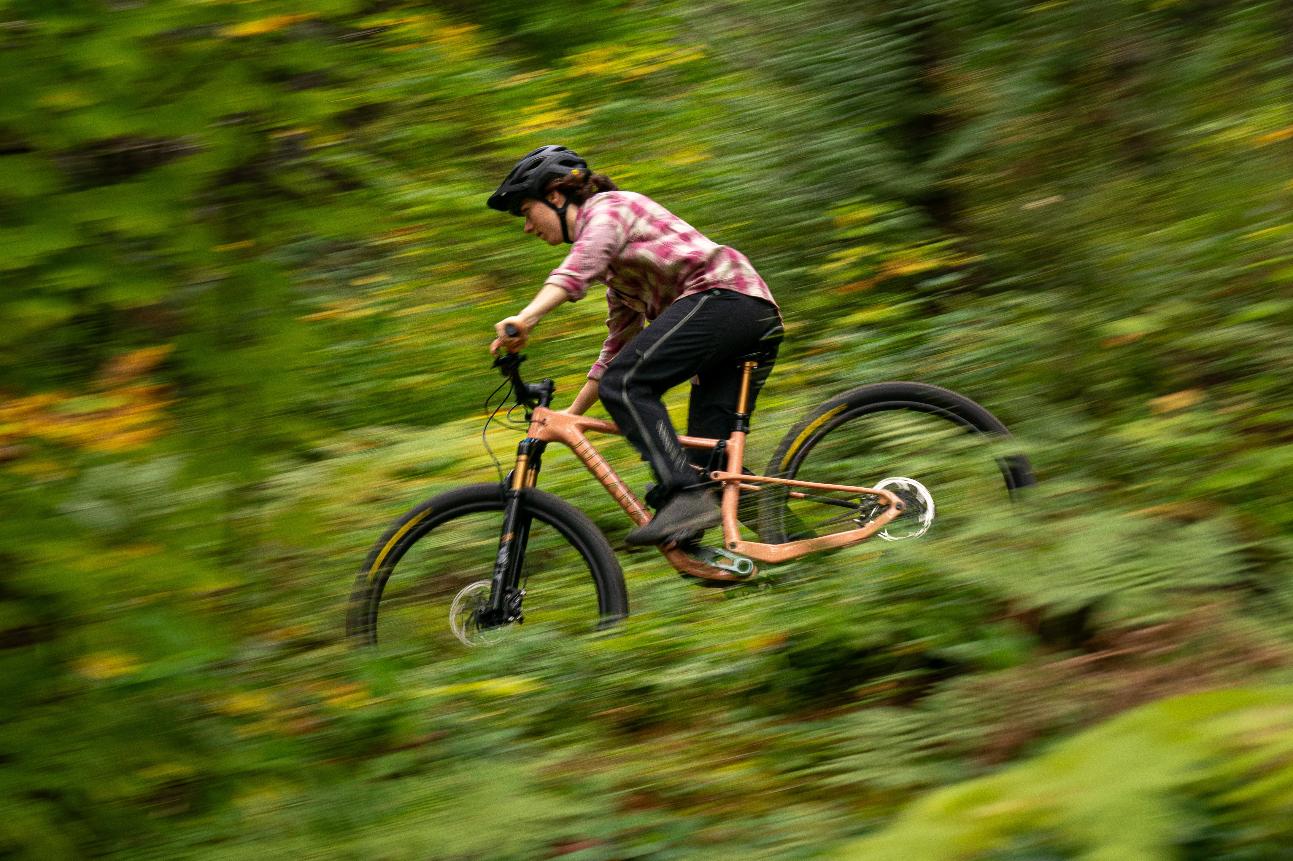 An action shot of a woman on a Juliana Furtado mountain bike as she rides through a forest trail, showcasing the bike's agility and performance on challenging terrain, available at Contender Bicycles.