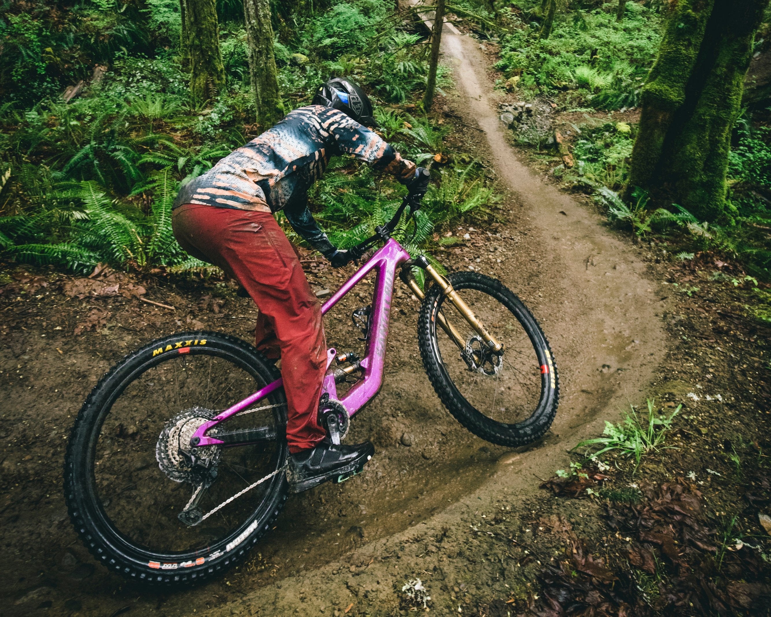 An action shot of a man leaning into a sharp turn on a Santa Cruz Heckler SL e-bike, sending dirt flying on a rugged trail, with dense trees and scenic surroundings, available at Contender Bicycles.