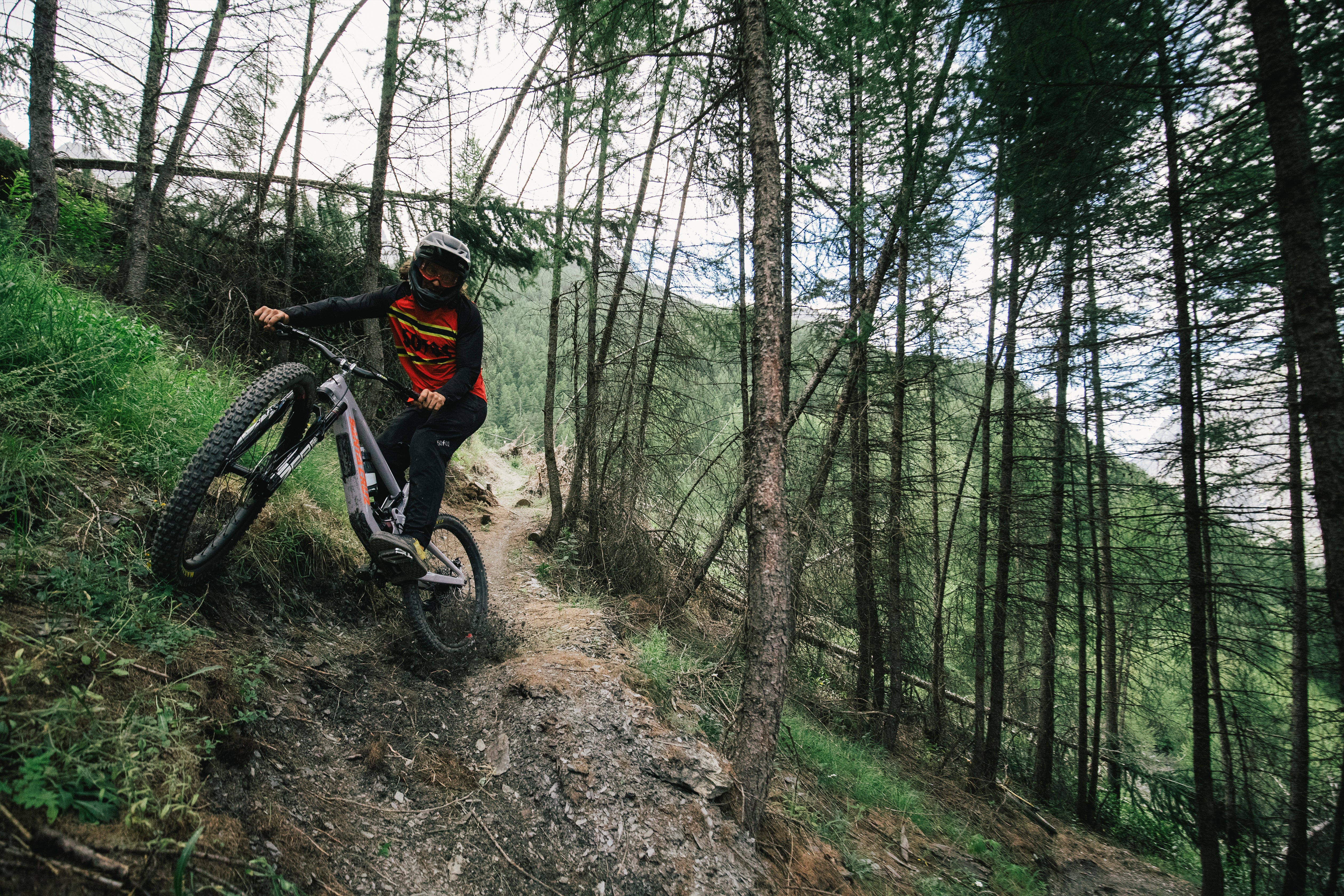 An action shot of a man riding a Santa Cruz Nomad through a forest trail, maneuvering over loose rocks and uneven terrain, highlighting the bike’s stability and performance in tough conditions, available at Contender Bicycles.