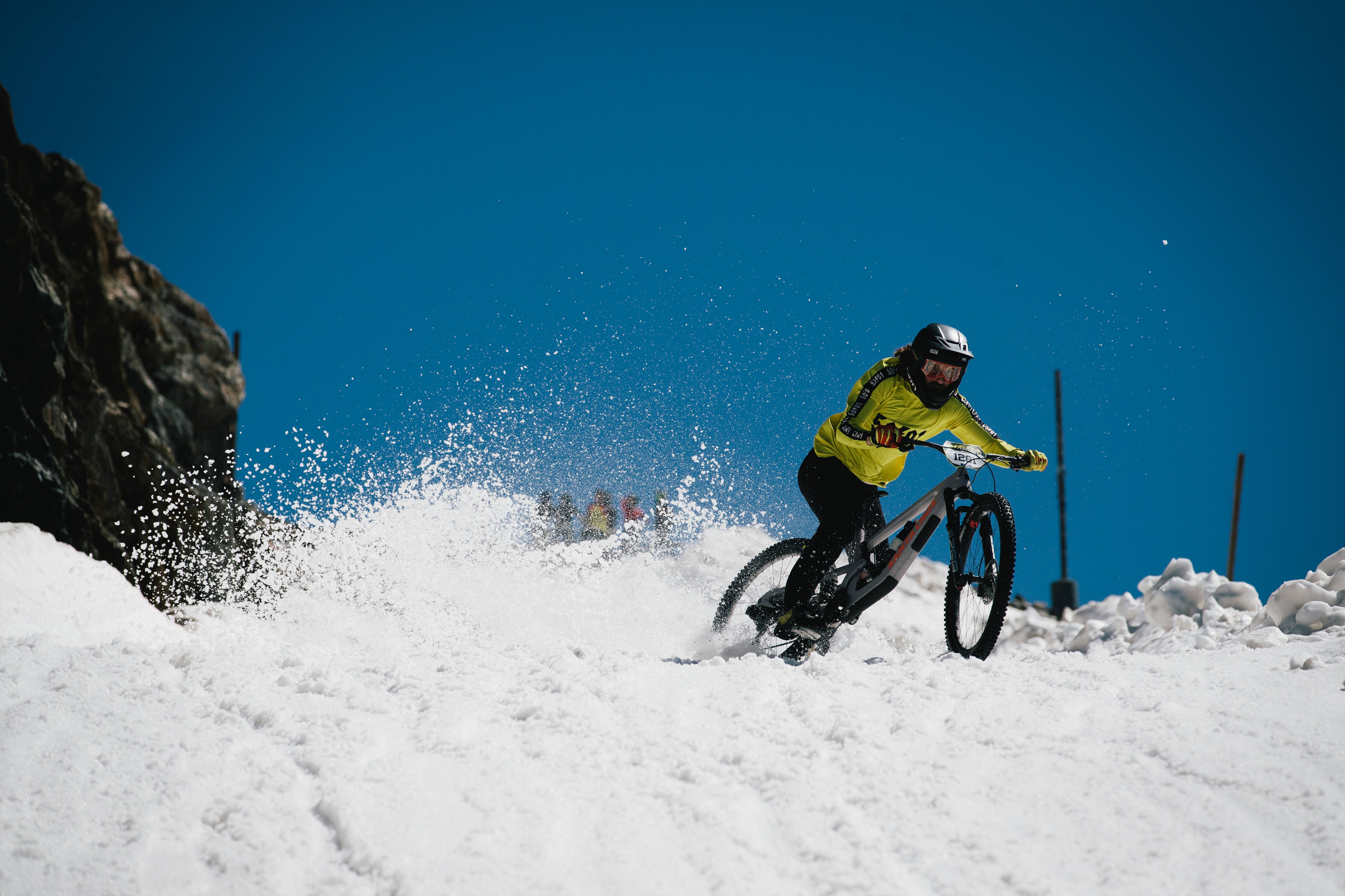 An action shot of a man riding a Santa Cruz Nomad down a snow-covered mountain trail, navigating through the snowy terrain with ease, showcasing the bike’s stability and performance in winter conditions, available to purchase at Contender Bicycles.