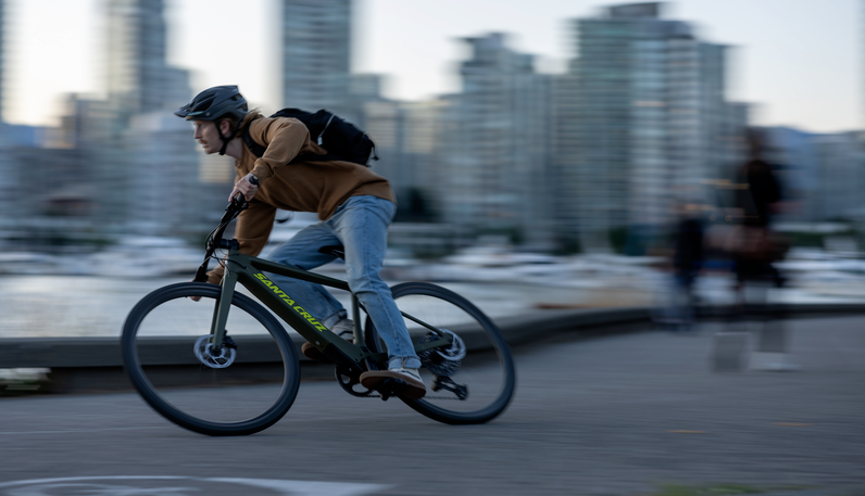 An action shot of a man riding a Santa Cruz Stigmata electric bike through a bustling city street, weaving through traffic and showcasing the bike’s agility and versatility in an urban environment, available at Contender Bicycles.