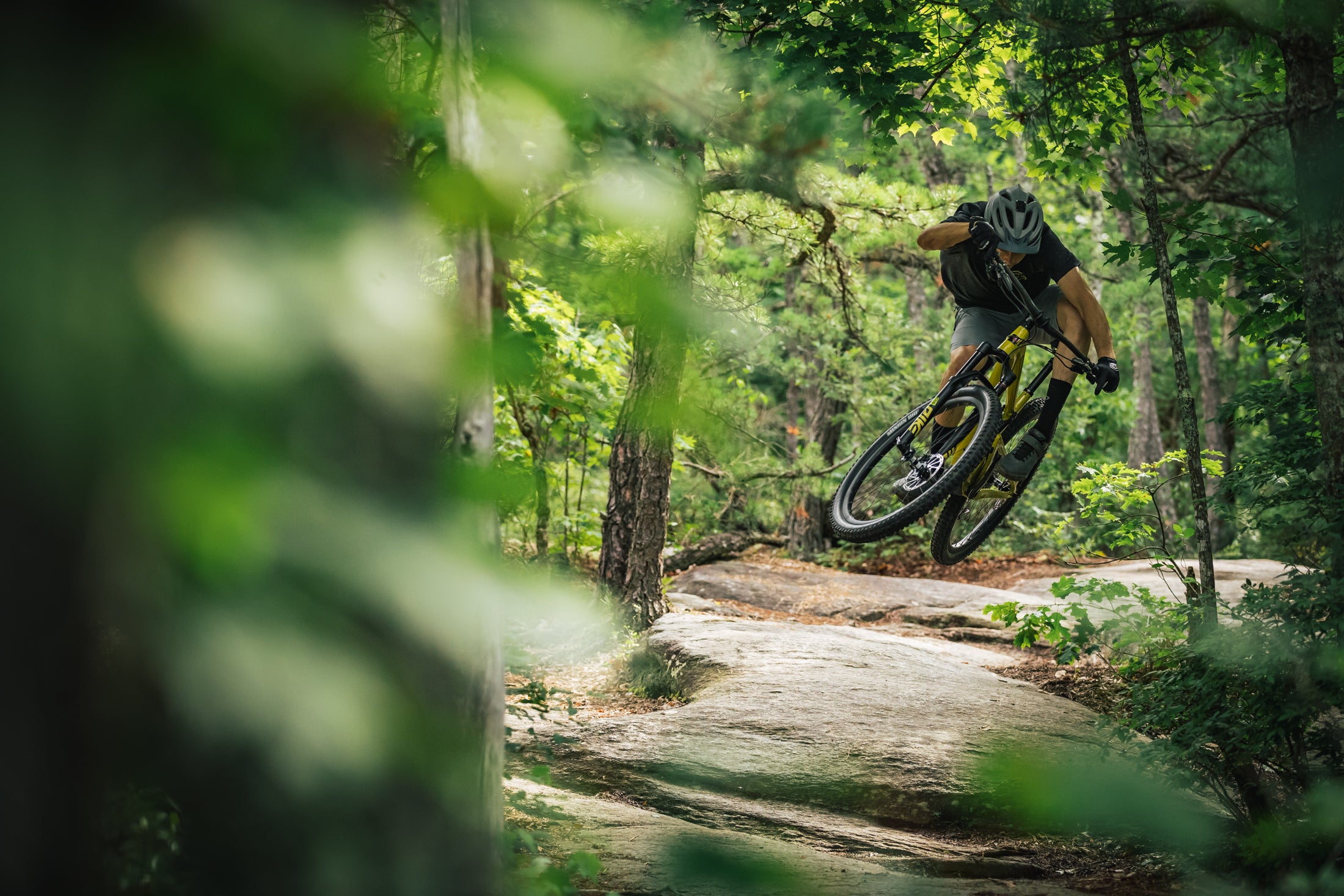 An action shot of a man riding a Santa Cruz Tallboy along a forest trail, tackling loose rocks and rough terrain, highlighting the bike’s stability and performance in demanding conditions, available at Contender Bicycles.