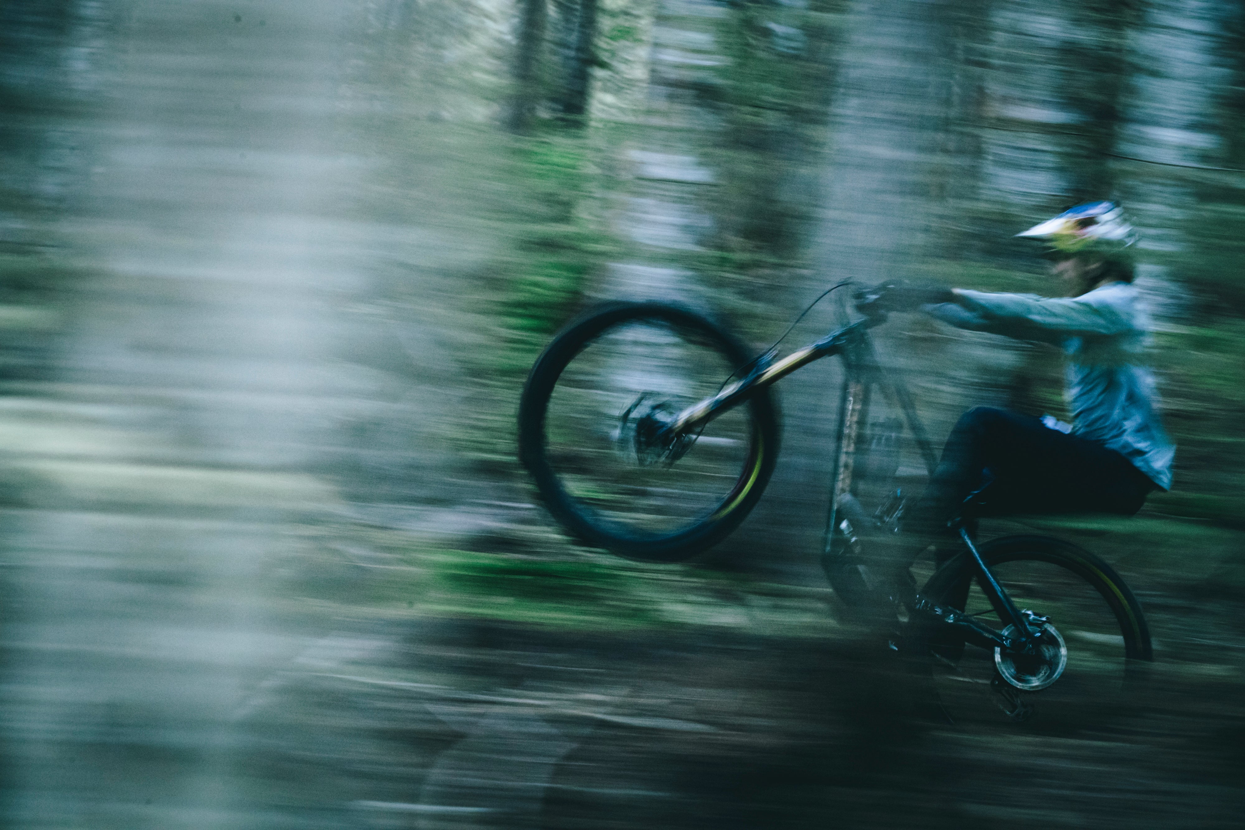 An action shot of a man performing a wheelie on a Santa Cruz Vala E-MTB through a forest trail, showcasing the bike’s power and agility on rough terrain, available at Contender Bicycles.