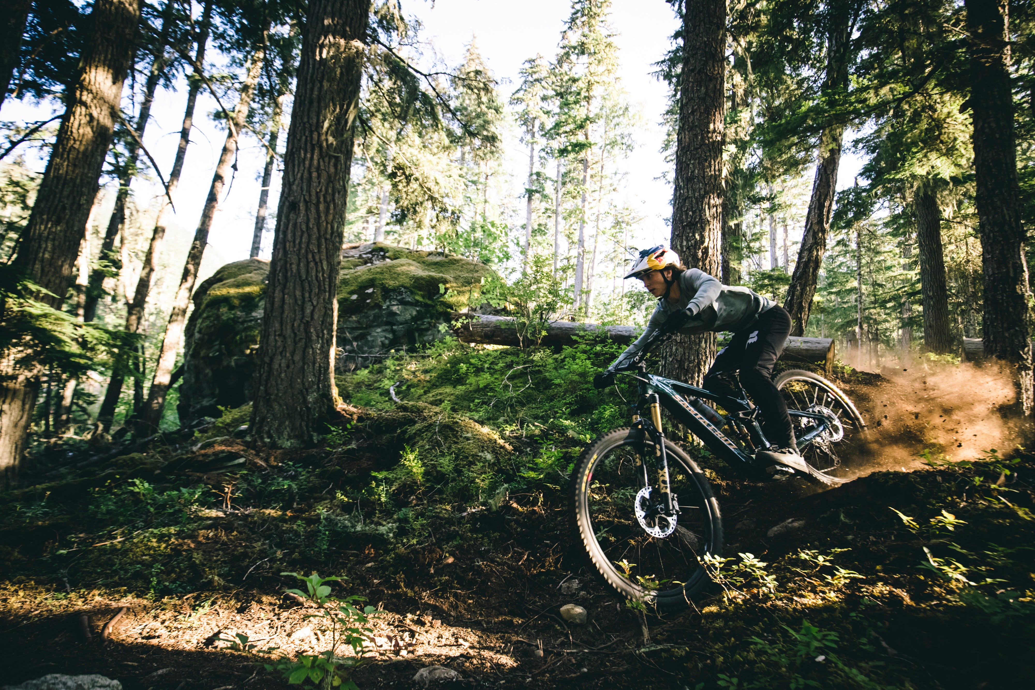 An action shot of a man pulling a wheelie on a Santa Cruz Vala E-MTB as he rides through a forest trail, demonstrating the bike's power and agility on challenging terrain, available at Contender Bicycles.