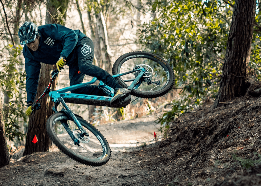 A man going off a jump on a dirt trail in the Forrest, riding the Scott Genius mountain bike