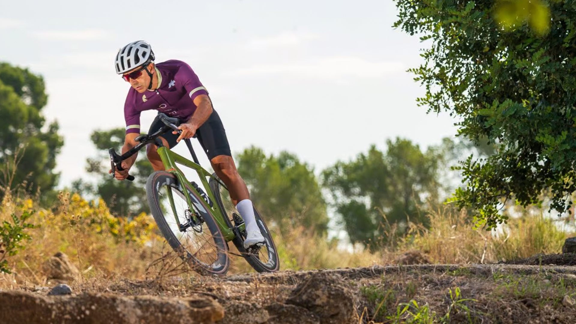 Person riding a bicycle on a dirt trail with trees in the background.