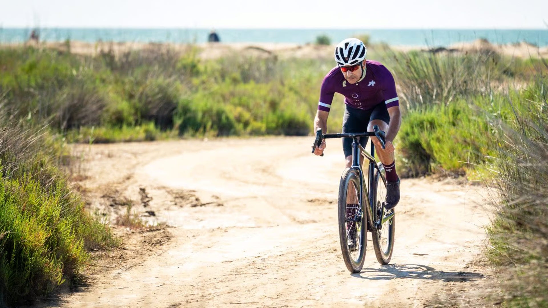 Cyclist in a purple jersey riding on a dirt path with ocean in the background