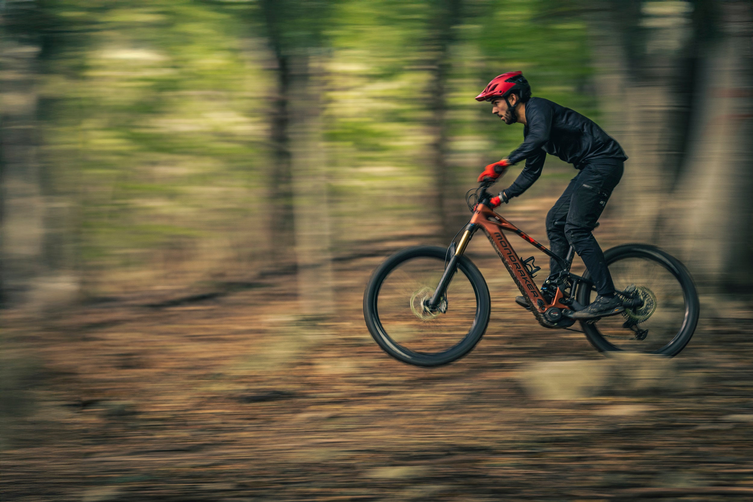 a man riding the Mondraker Craftey Electric mountain bike through a forest. 