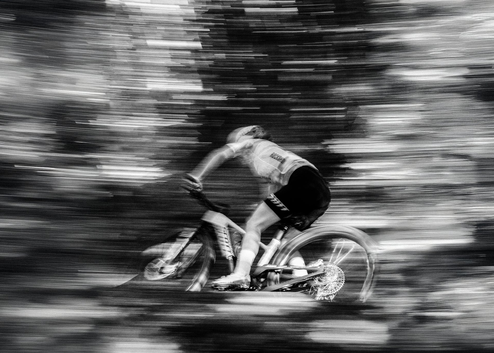 Black and white image of cyclist riding through a forest.