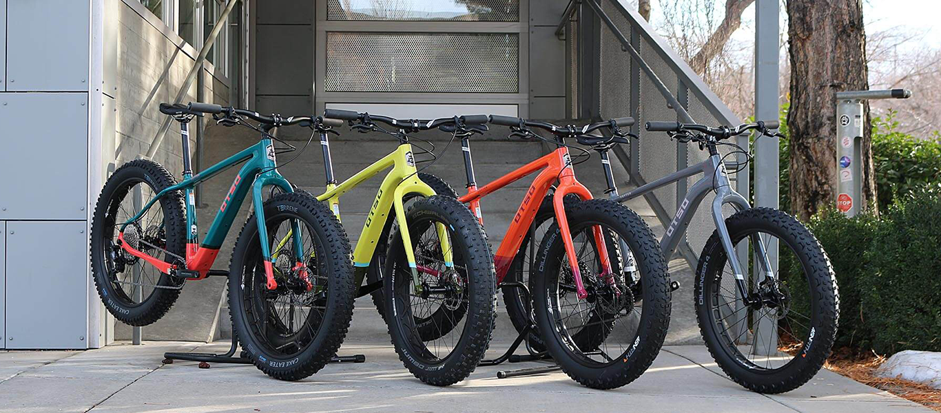 colorful otso fat bikes lined up in front of a grey staircase in front of a bike shop