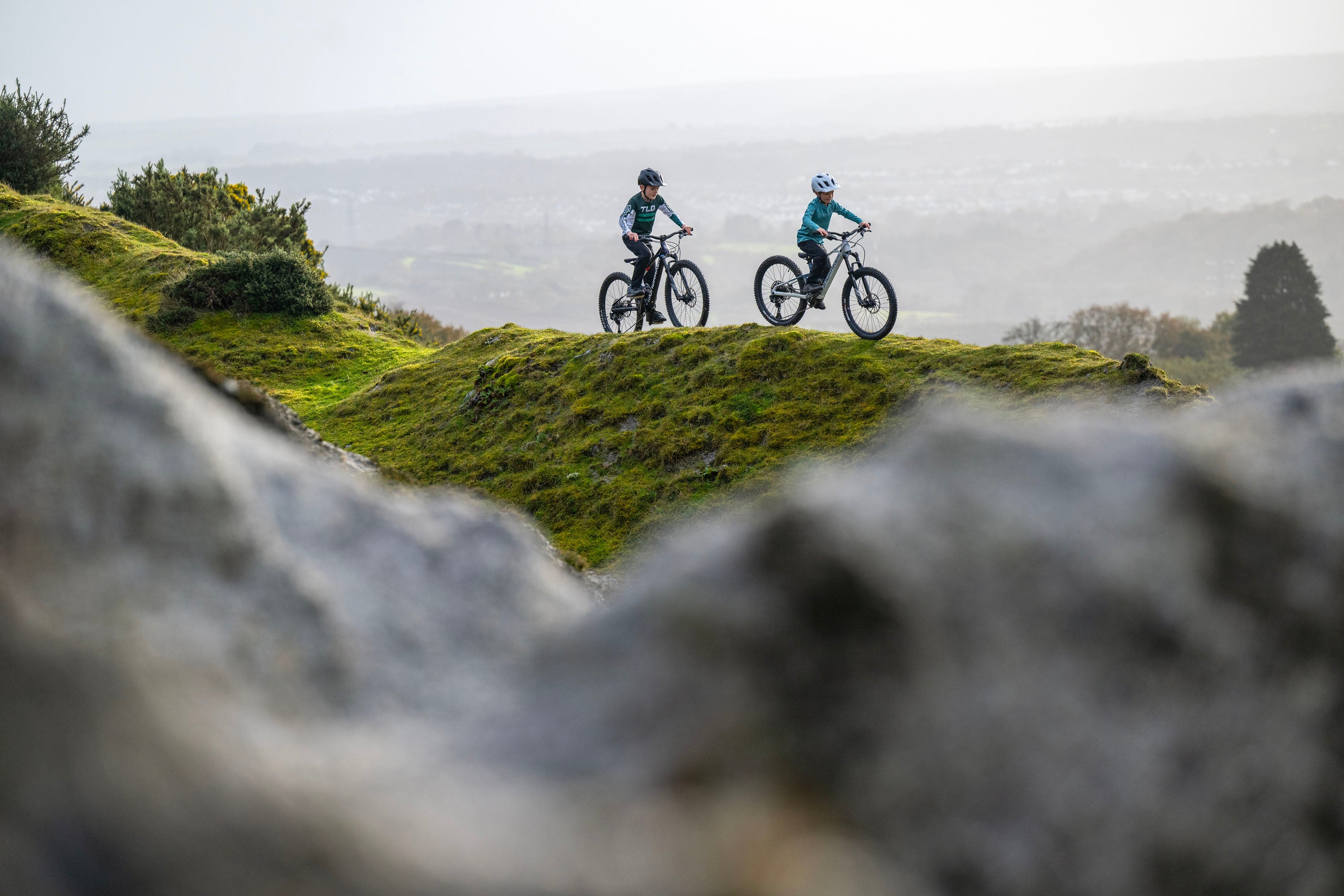 Two children riding the Mondraker F play mountain bike on a ridgeline together. Available at Contender Bicycles.