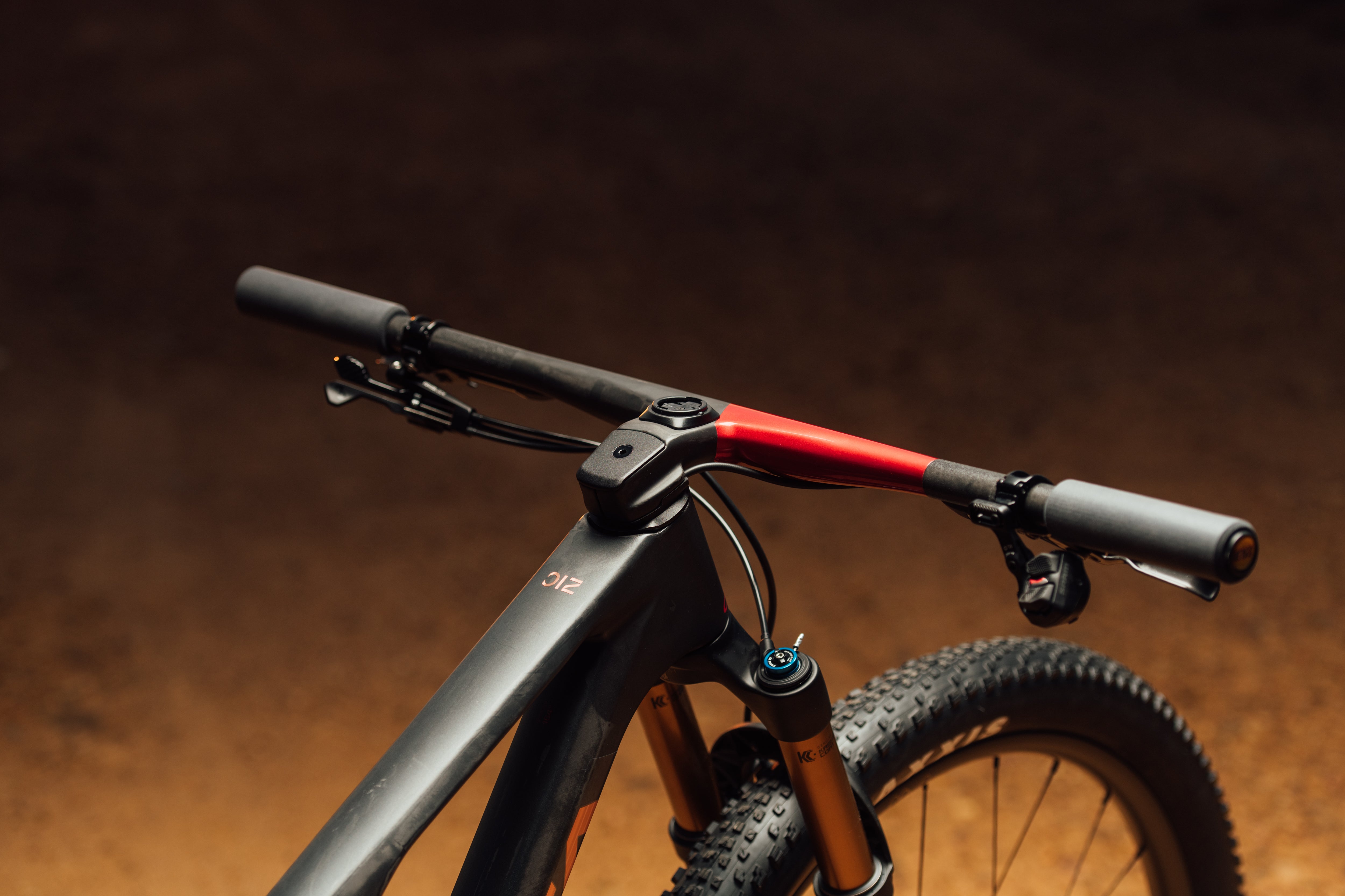 The handle bars of a 2025 orbea oiz in black and red paint with a dirt background.