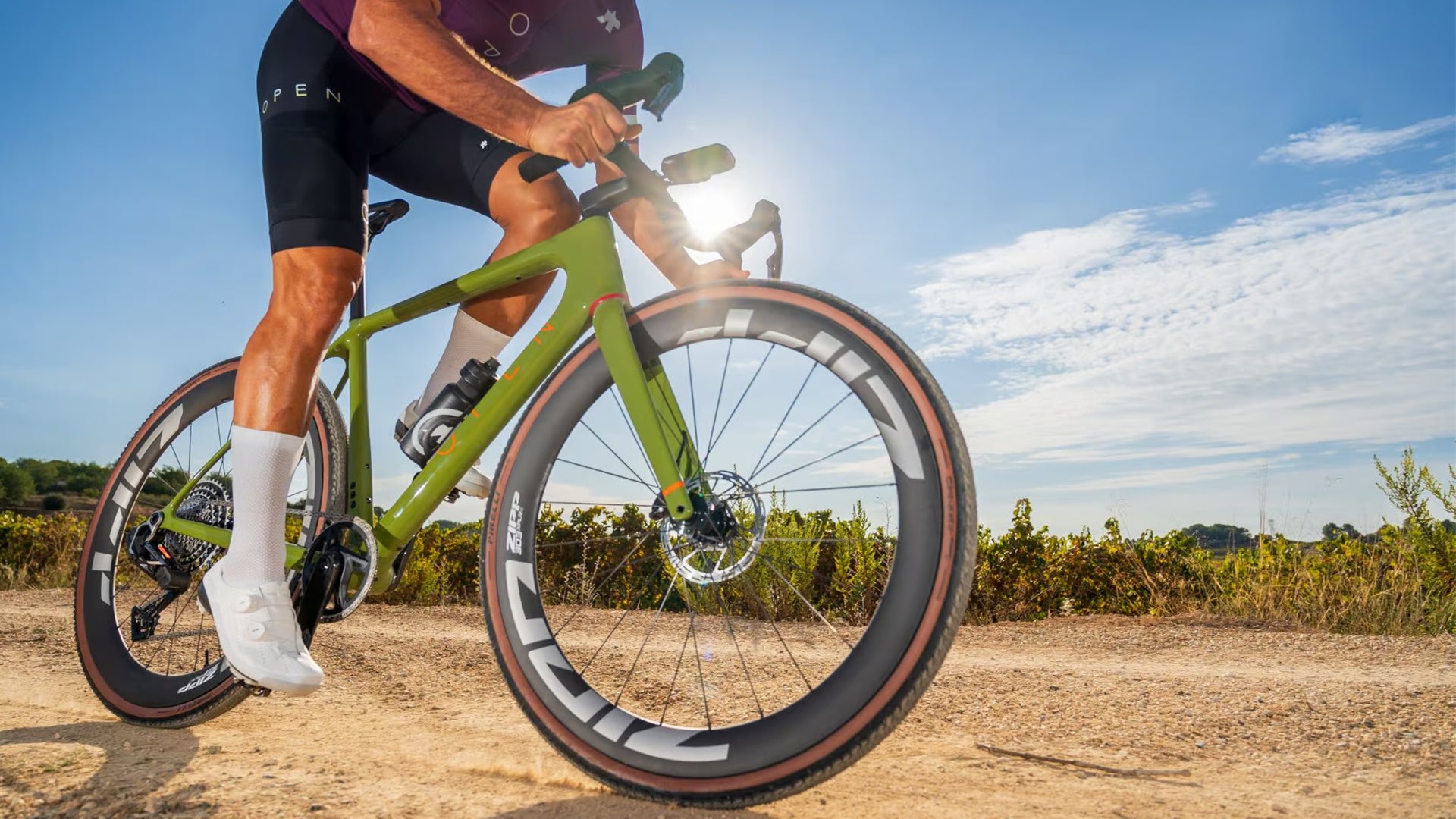 A man riding a green open up gravel bike on a dirt road. 