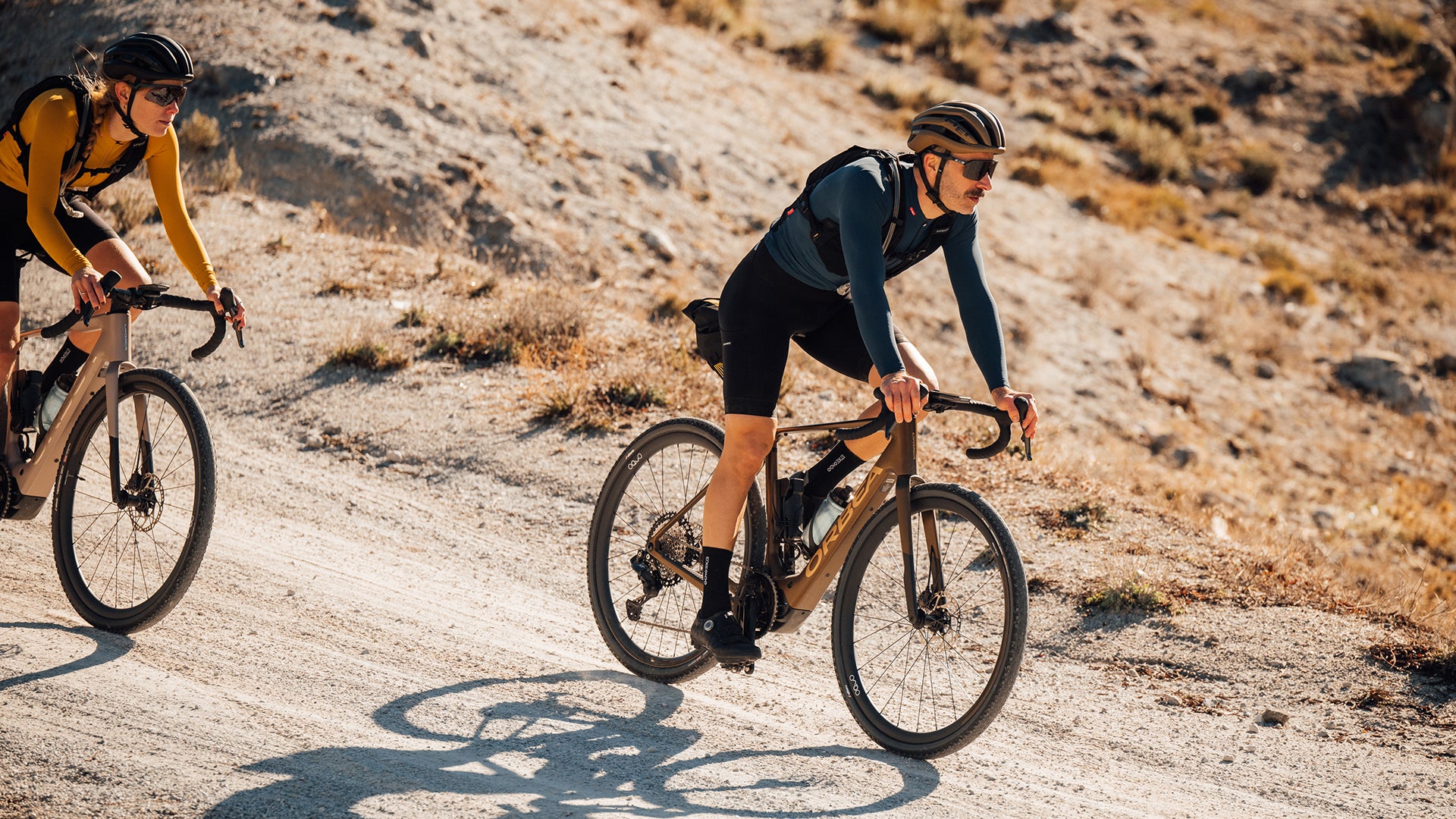 Two people riding the orbea denna electric gravel bike on some dirt roads. 