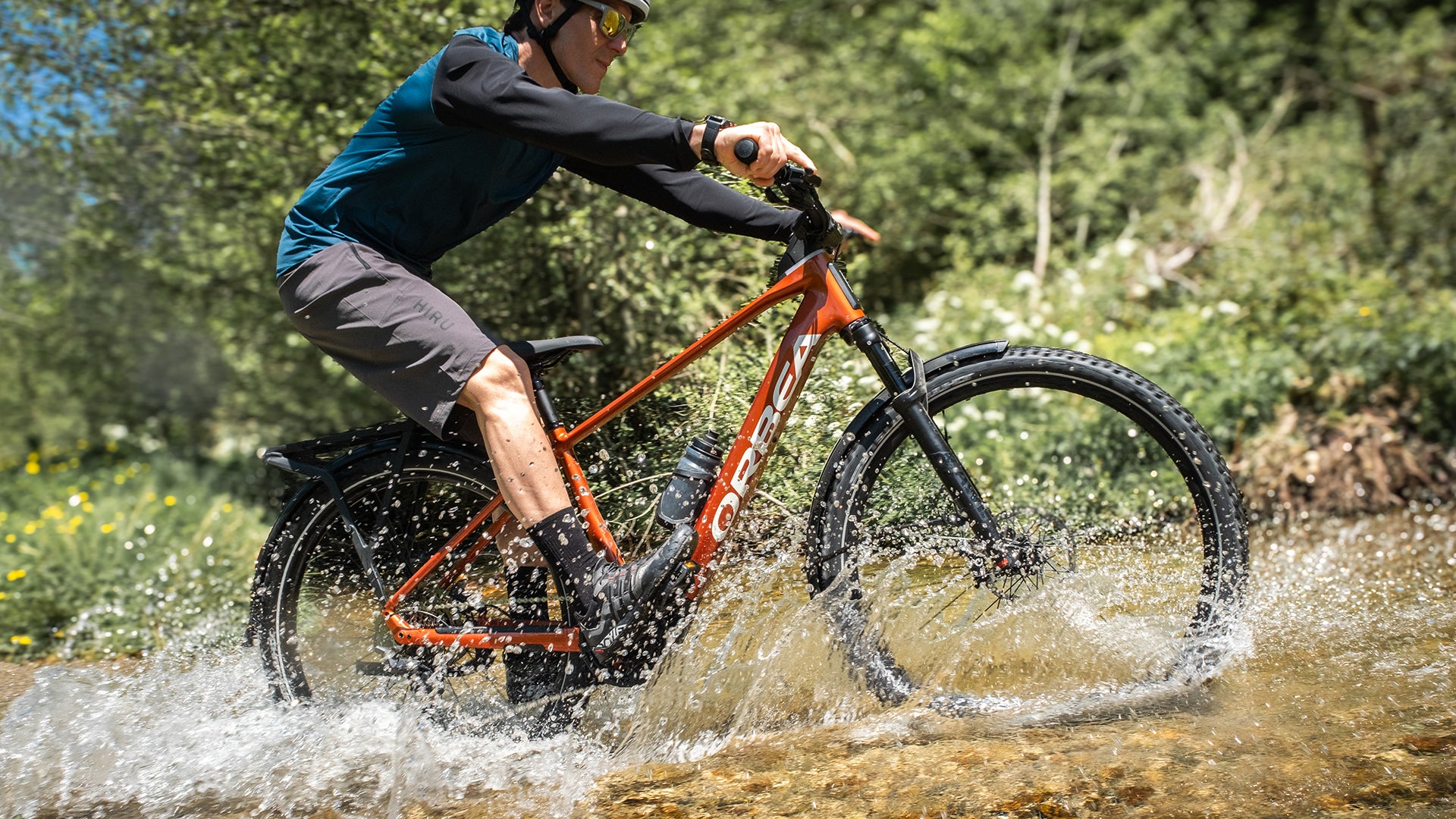 a man riding an orbea kemen electric bike through a river. 
