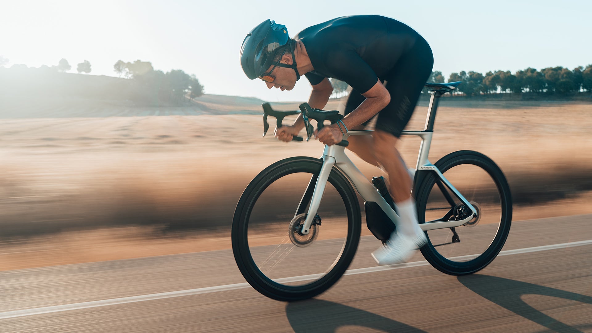 a man riding the orbea orca aero road bike in front of some farming fields. 