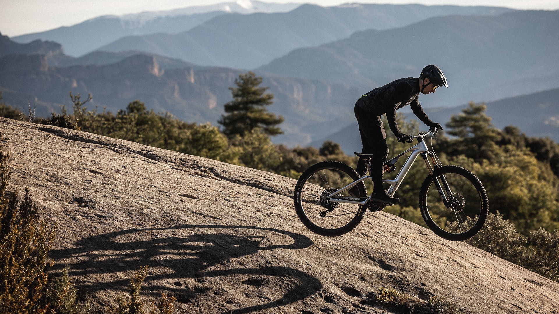 A man riding an electric orbea rise mountain bike on some rocks. 