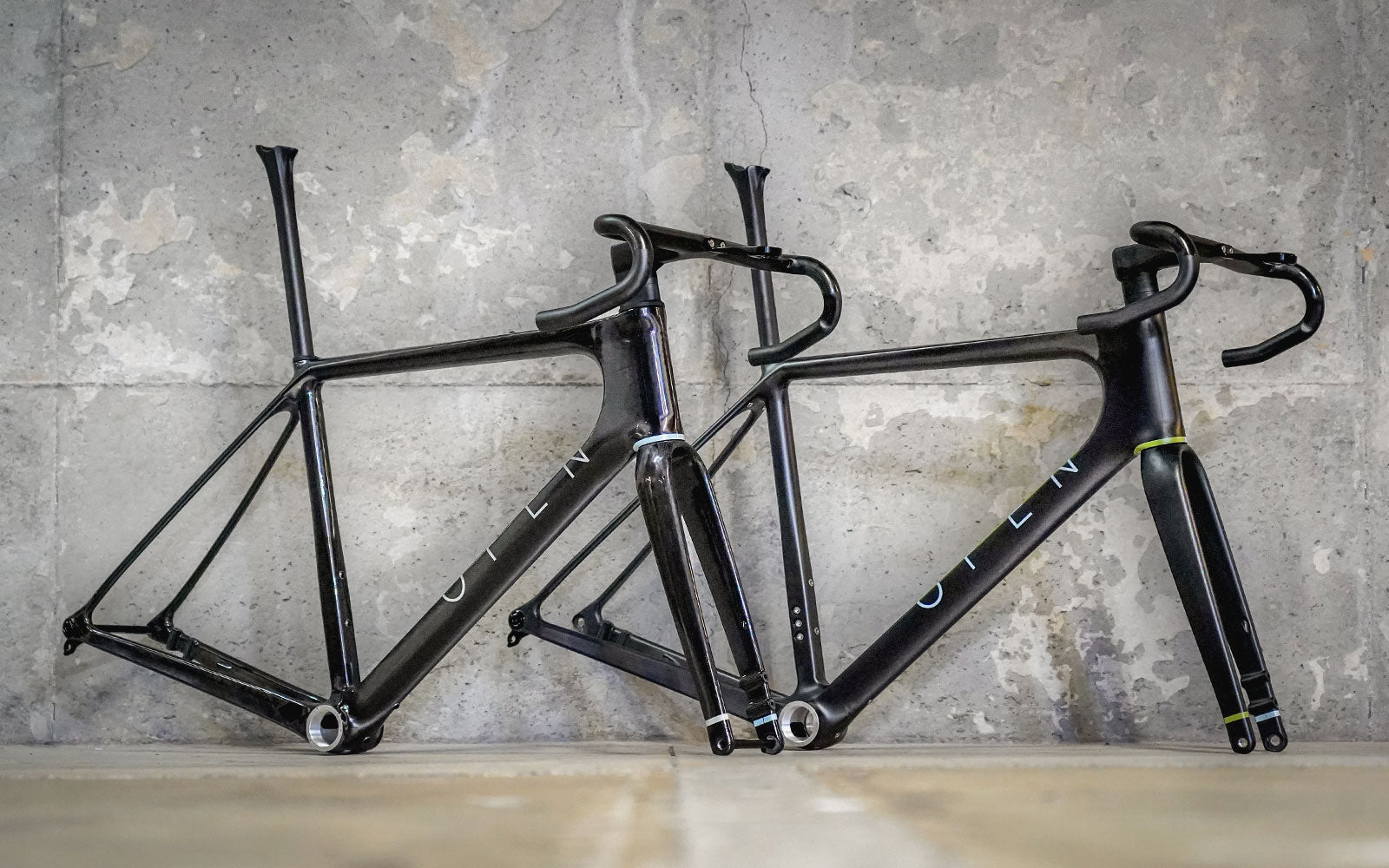 OPEN Concept (left) and UPPER 2.0 (right) framesets displayed against a concrete wall. Available at Contender Bicycles