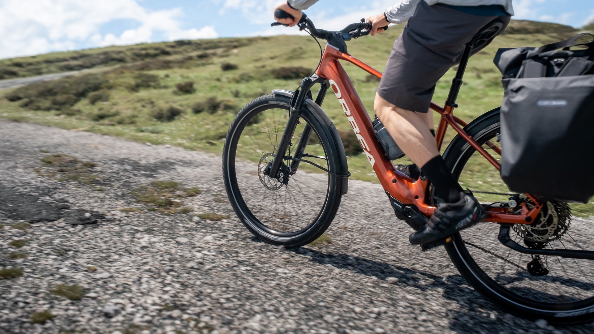 A man riding an orange orbea kemen electric bike up a hill. 
