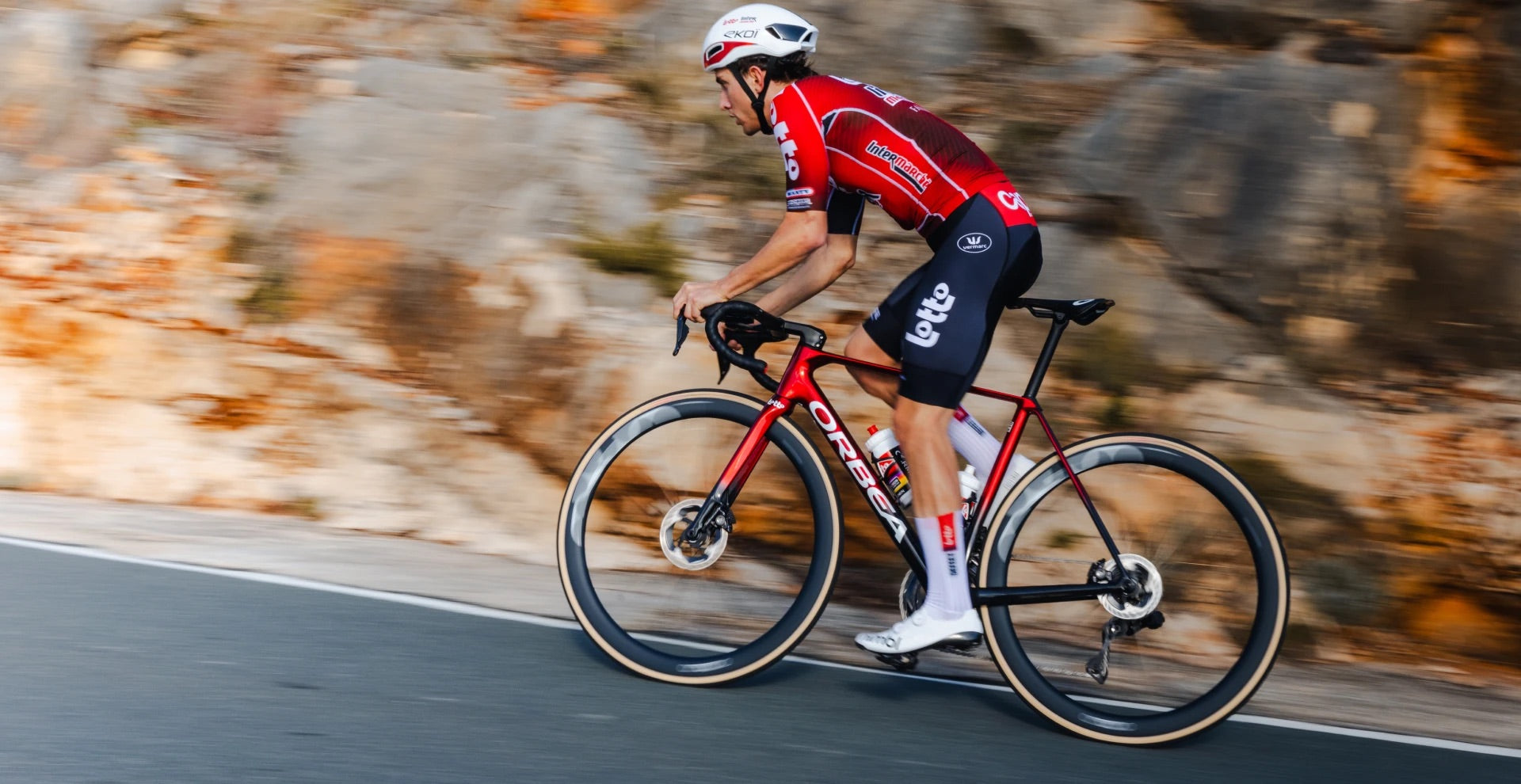 a Man riding a red orbea orca road bike up a hill in a red jersey