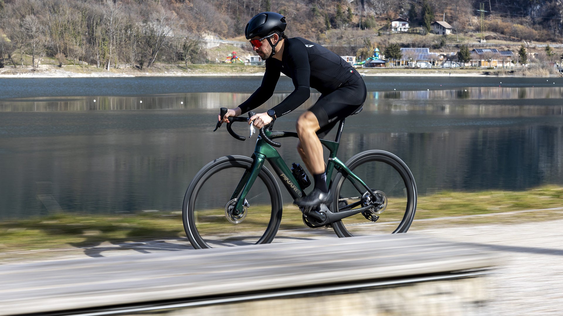 A Man riding the pinarello Nytro road electric bike on a paved road with a lake