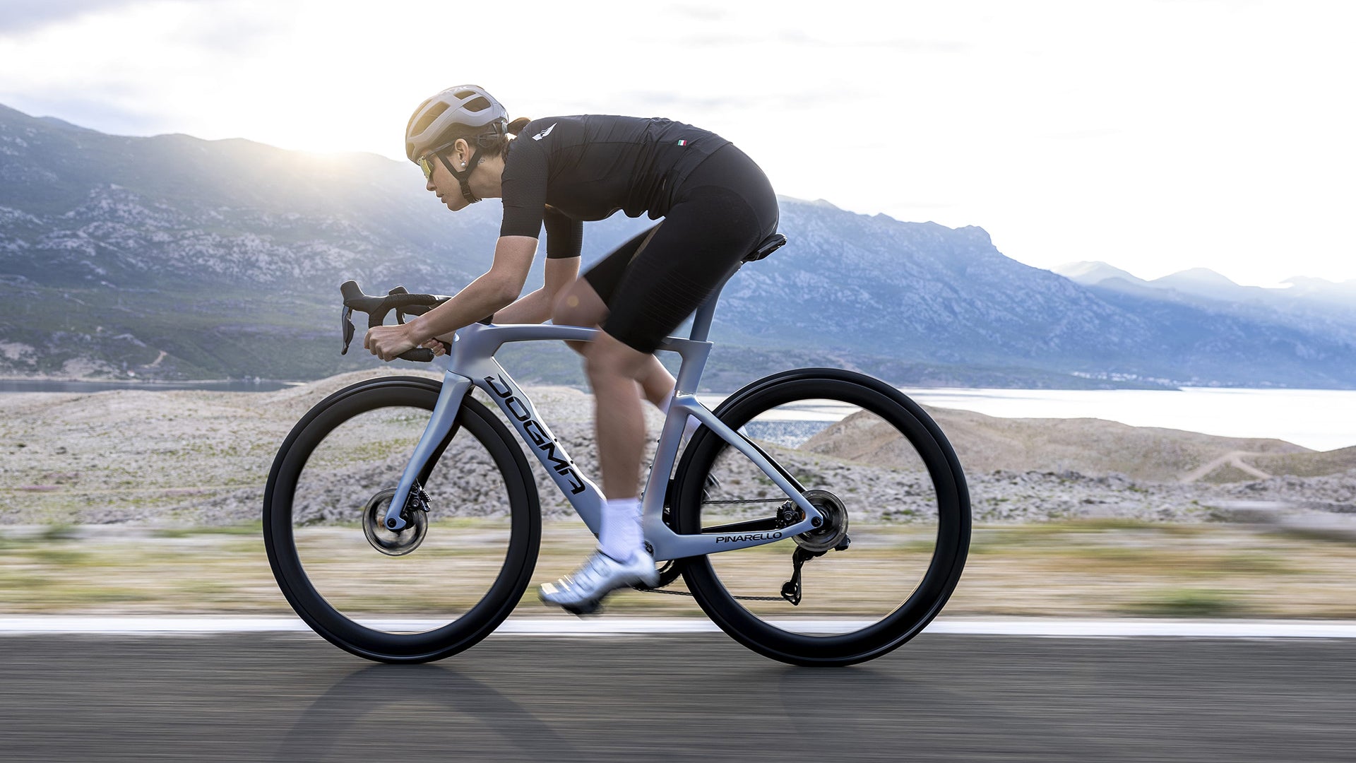 A woman riding a pinarello dogma road bike against a mountain and lake background