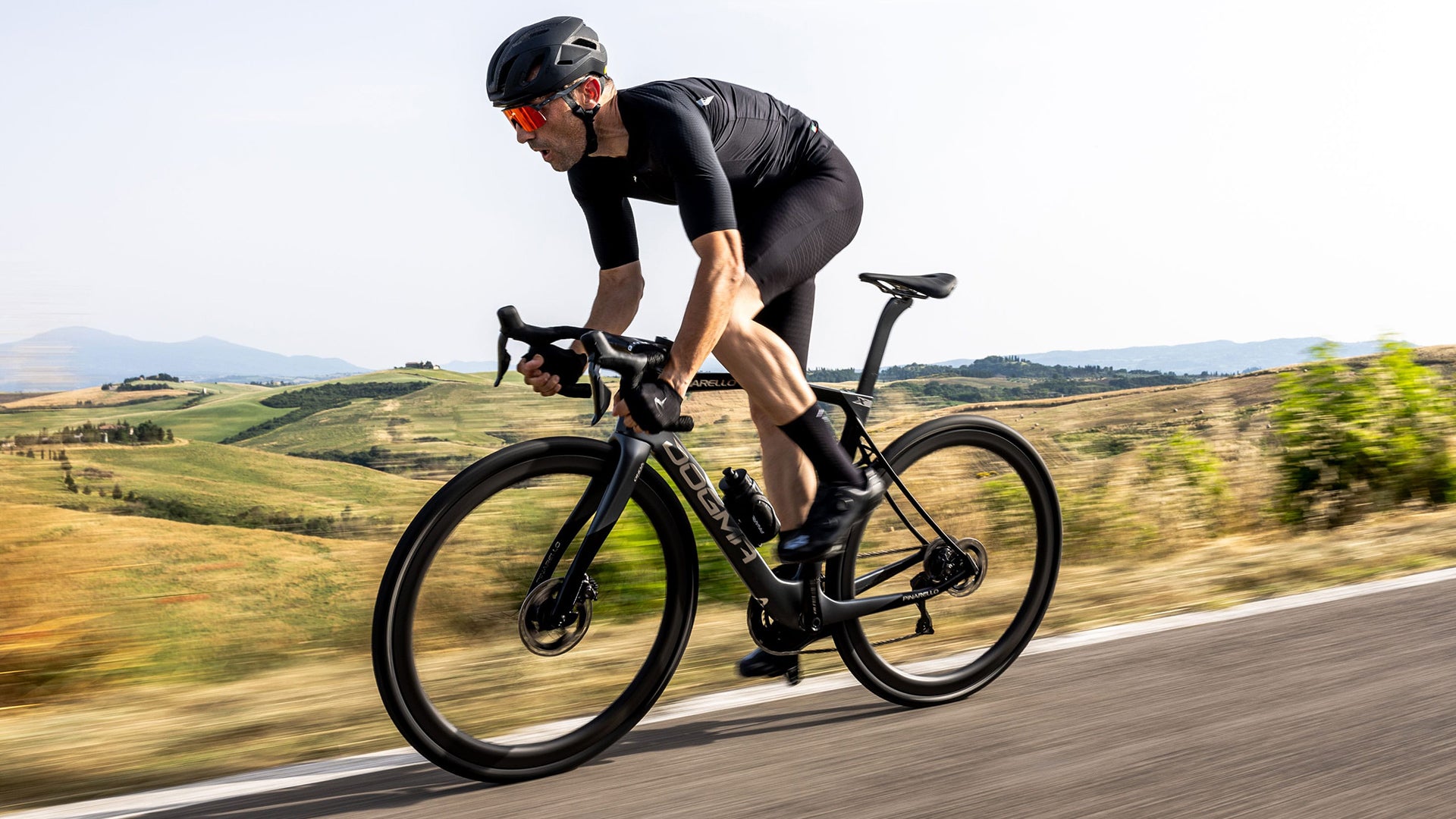 A Man riding the Pinarello Dogma x Road bike against some rolling hills