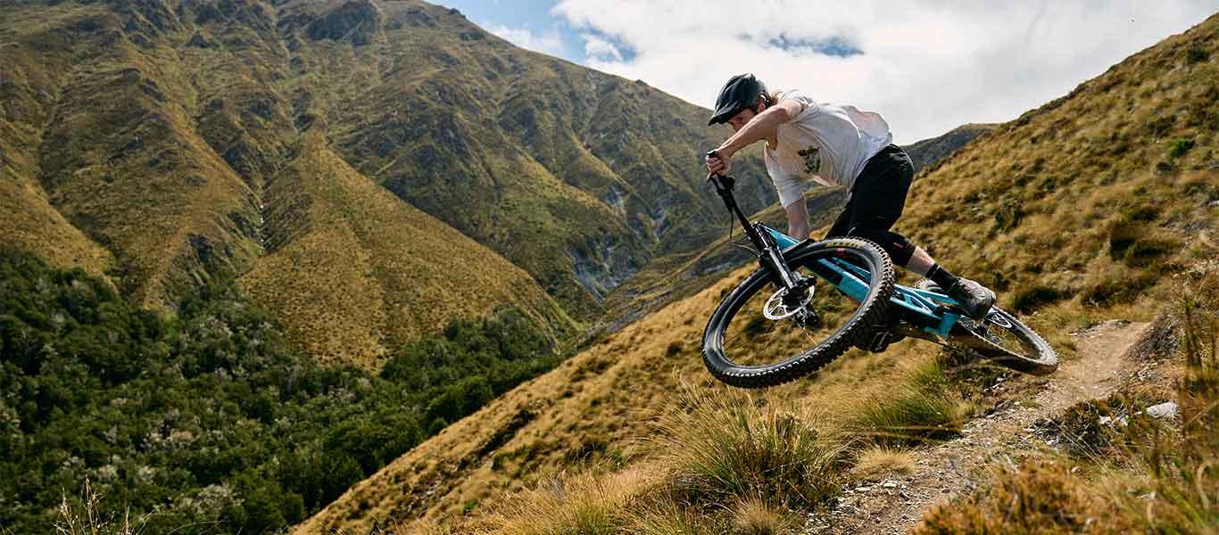 Person riding a mountain bike on a trail with mountains in the background