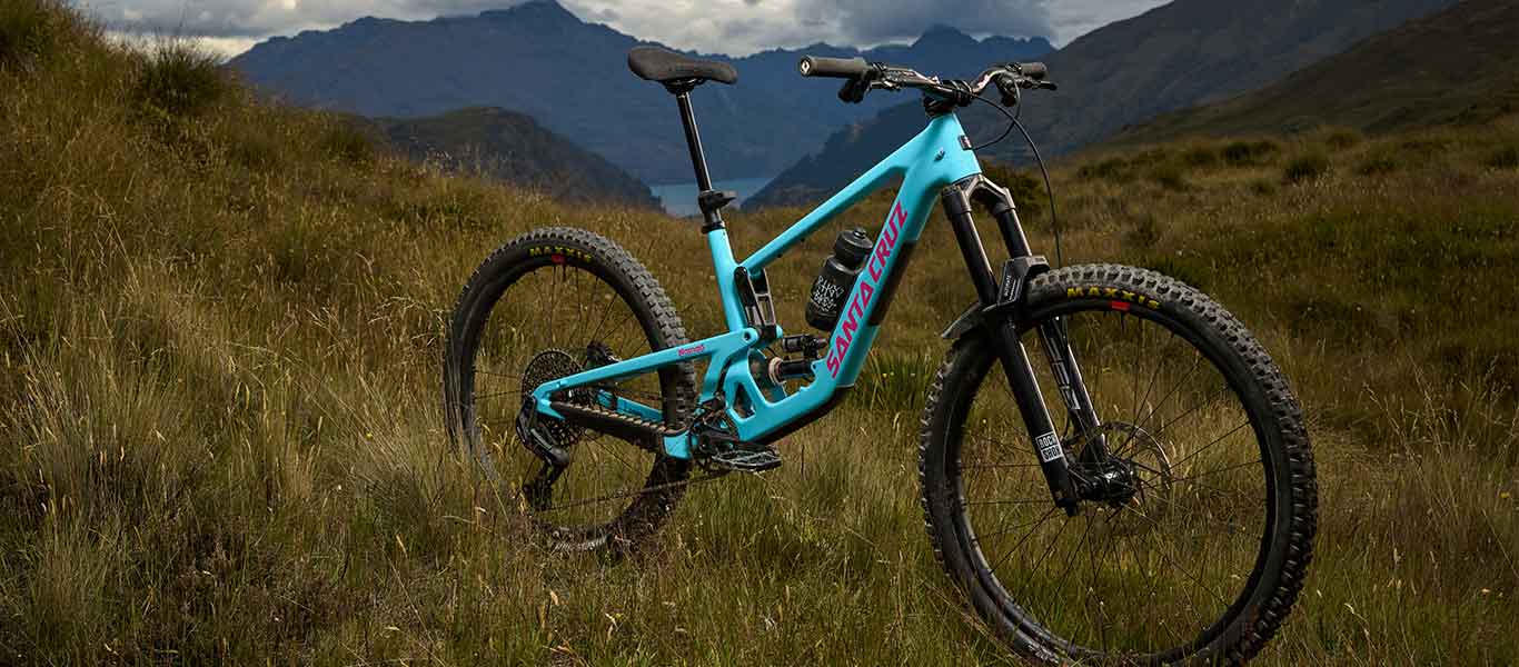 Turquoise mountain bike on a grassy hill with mountains in the background