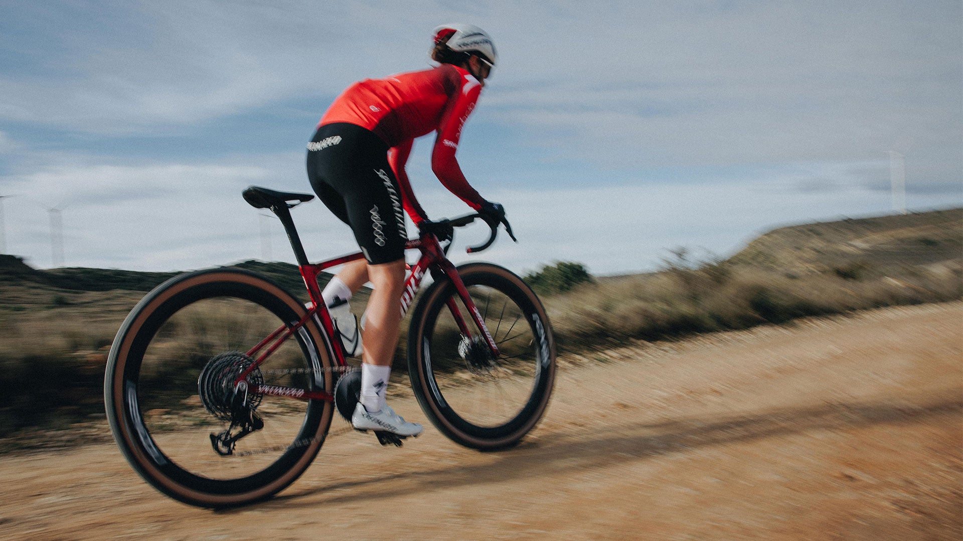 Cyclist in red jersey riding a bicycle on a dirt road with a clear sky.