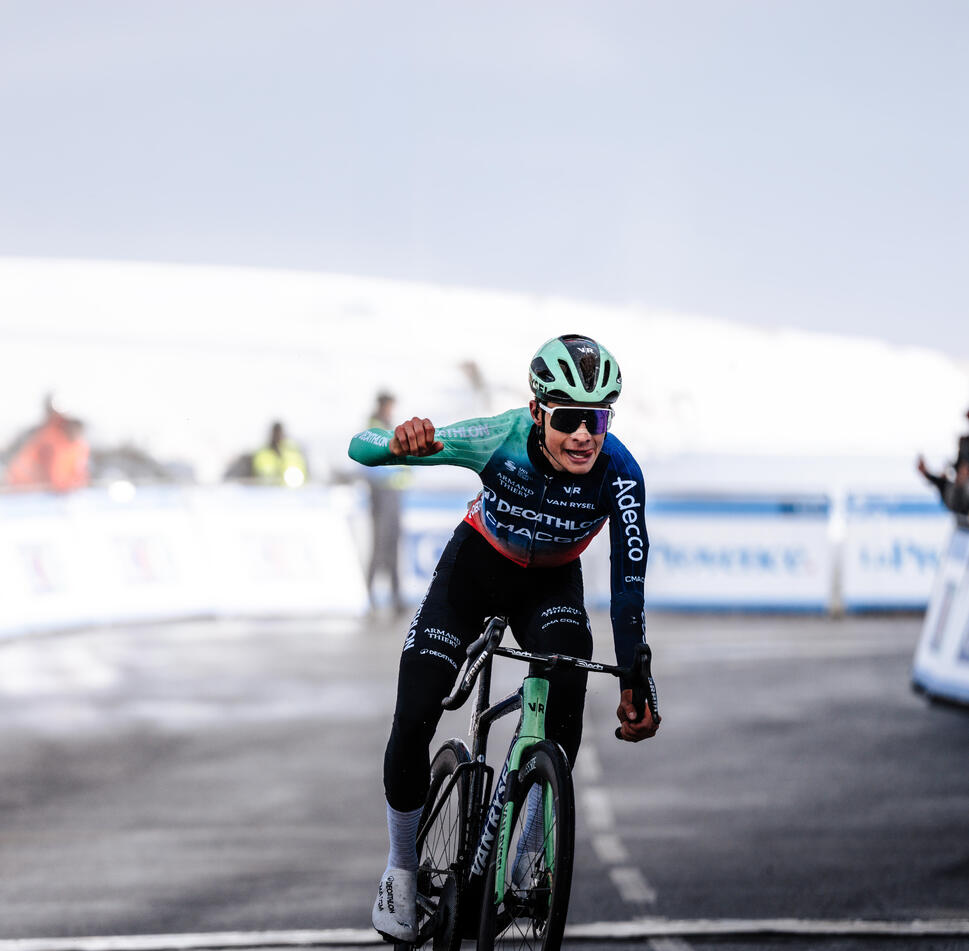 Cyclist in a racing outfit with a helmet and sunglasses, riding a bicycle on a road race track.