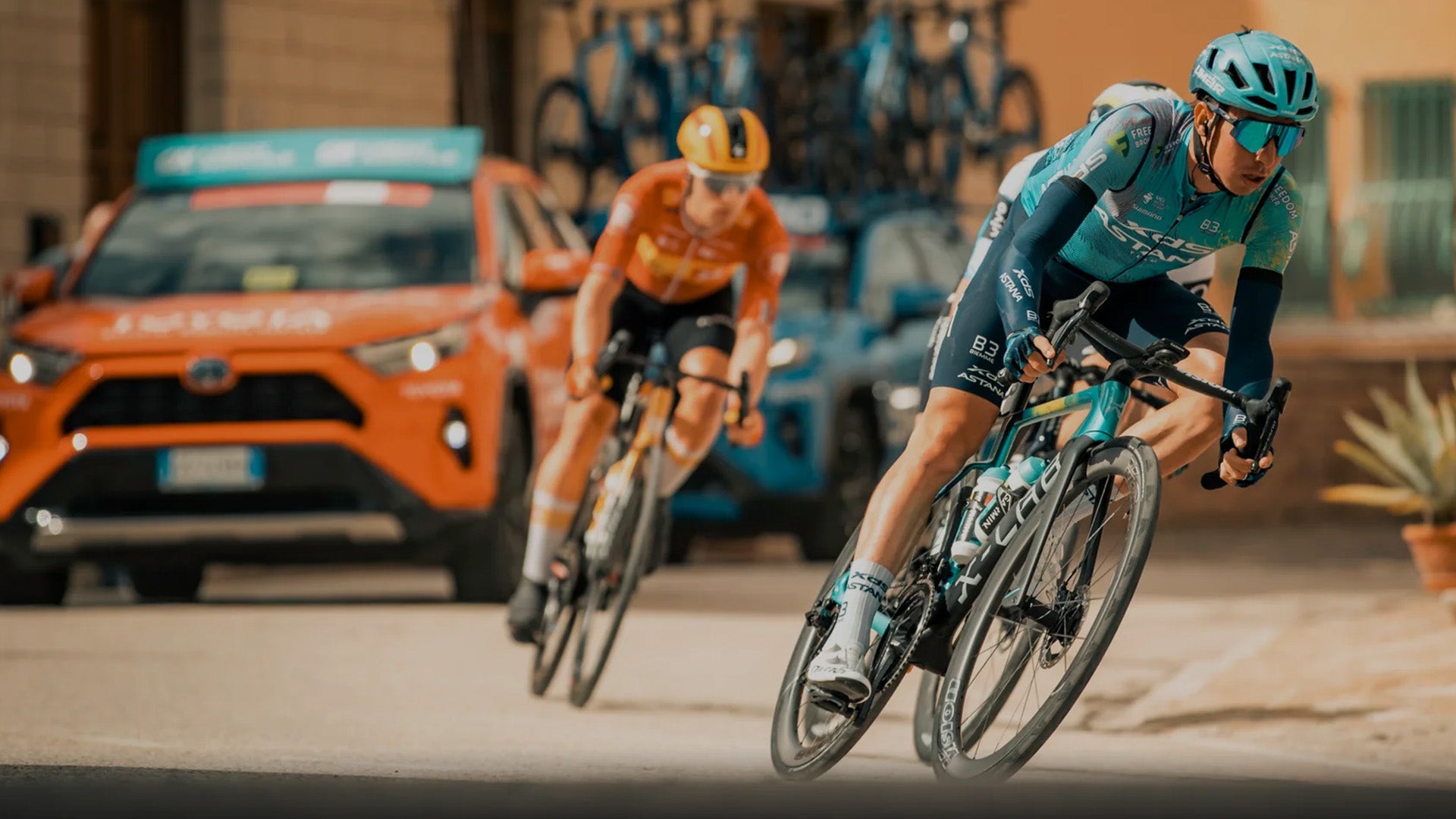 Two cyclists racing on a road with a support vehicle in the background.