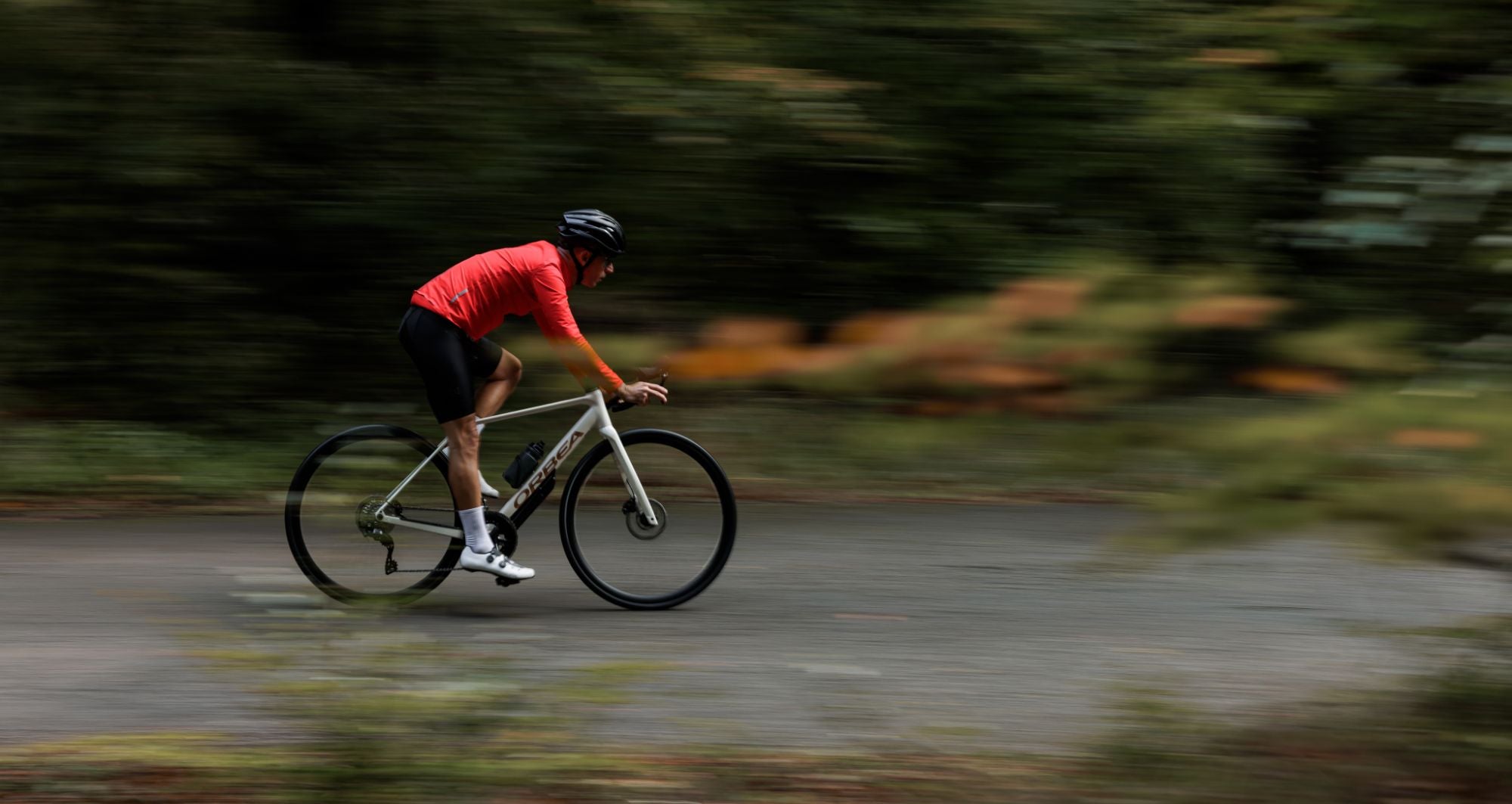 A man in a red shirt is riding the Orbea Avant Road bicycle on a road in the forest.