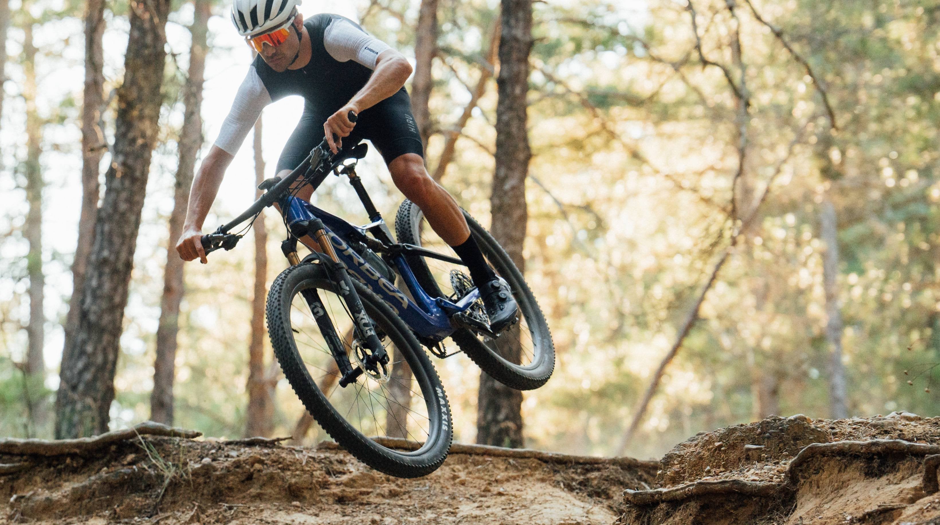 A man riding the Orbea Oiz Mountain bike with blue and black paint on a dirt trail. 