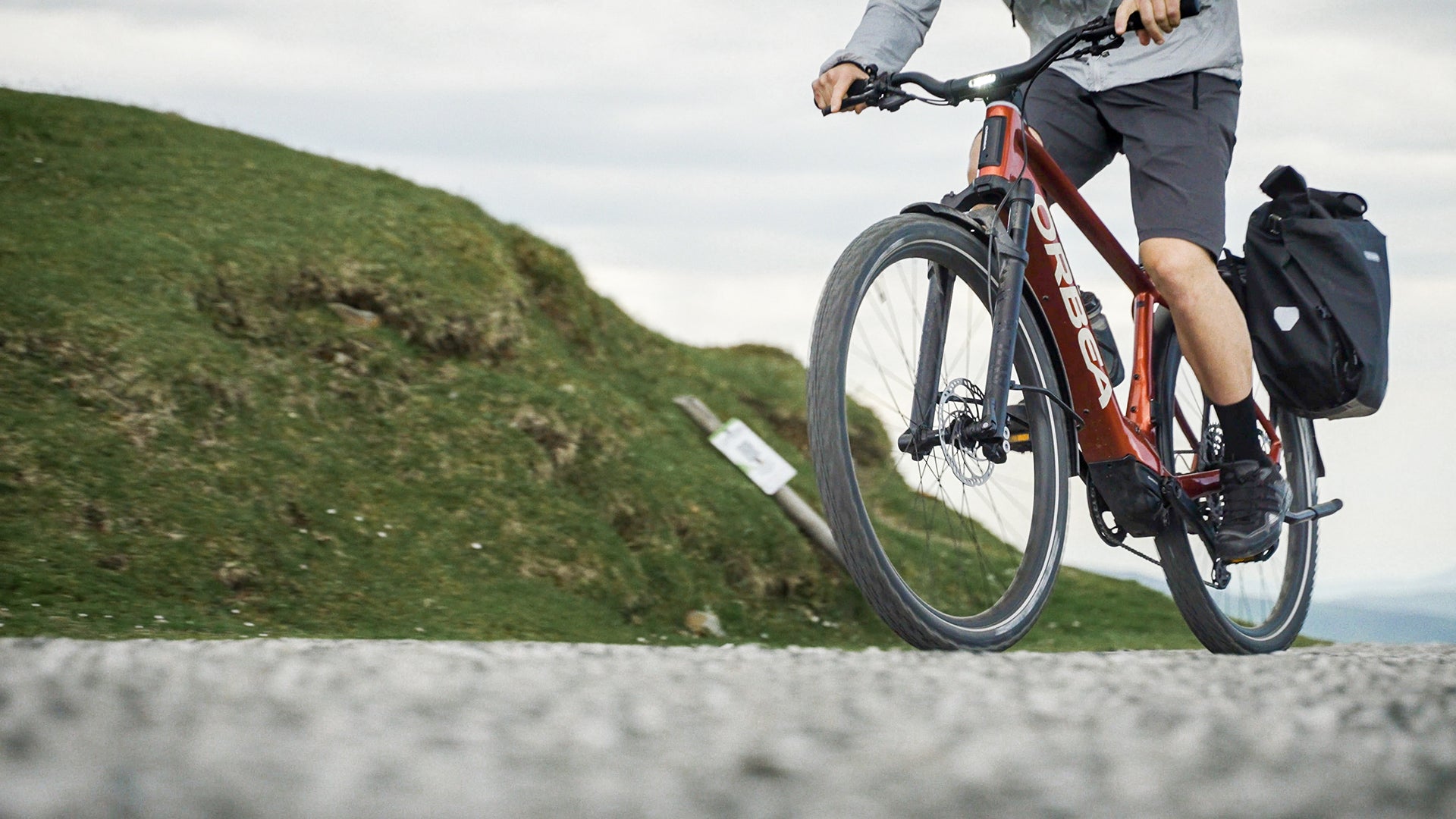 A man riding an orange orbea kemen electric bike up a hill. 