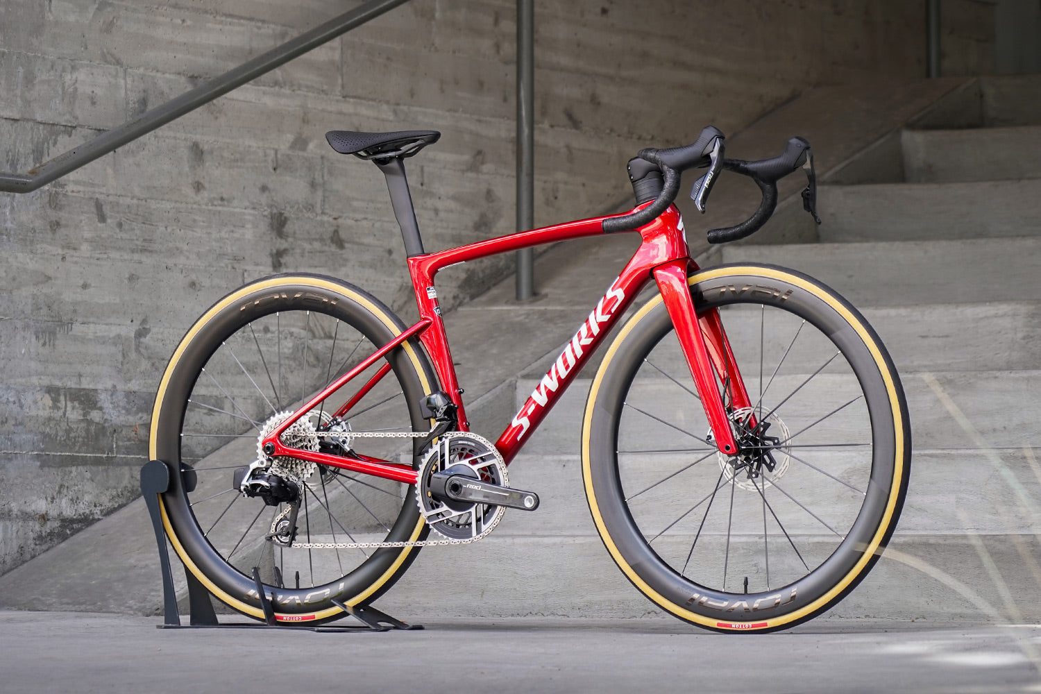 Red bicycle with black components leaning against a concrete wall.